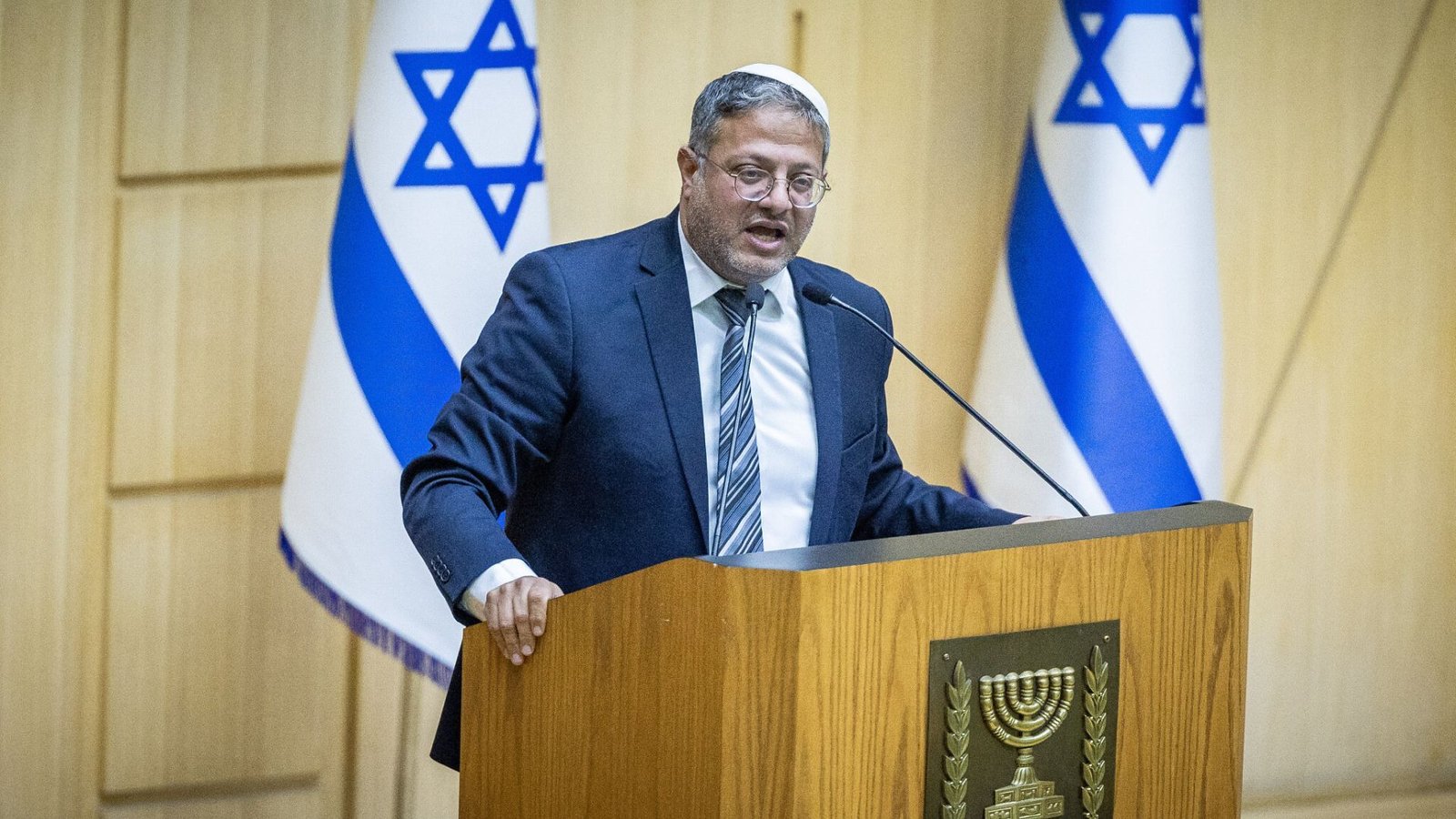 O ministro de segurança nacional, Itamar Ben-Gvir, ao centro com um terno e atrás de uma tribuna no congresso israelense.