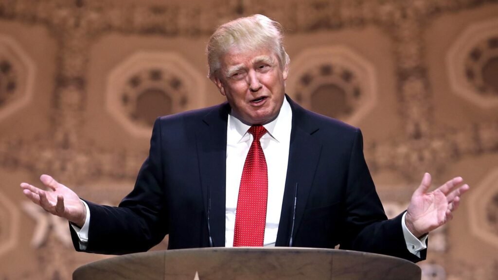 Após petróleo, ouro da Venezuela deve ir para os Estados Unidos Ao centro, o presidente Donald Trump, o presidente dos EUA que negociou o ouro. Ele é um homem branco, com a pele levemente alaranjada e cabelo branco. Usa um turno preto, gravata vermelha e camisa social branca.